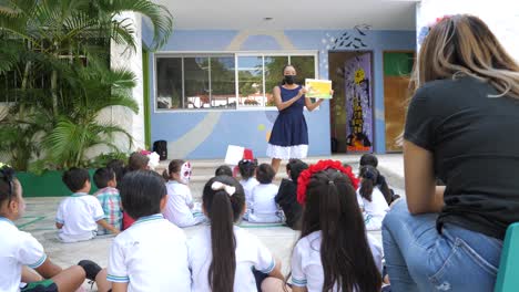 teacher wearing masks telling a story to a group of children in a private kindergarten at covid and day of the dead time