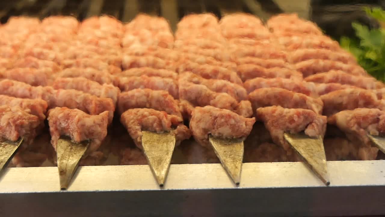 File di kebab di carne macinata cruda su spiedini di metallo.