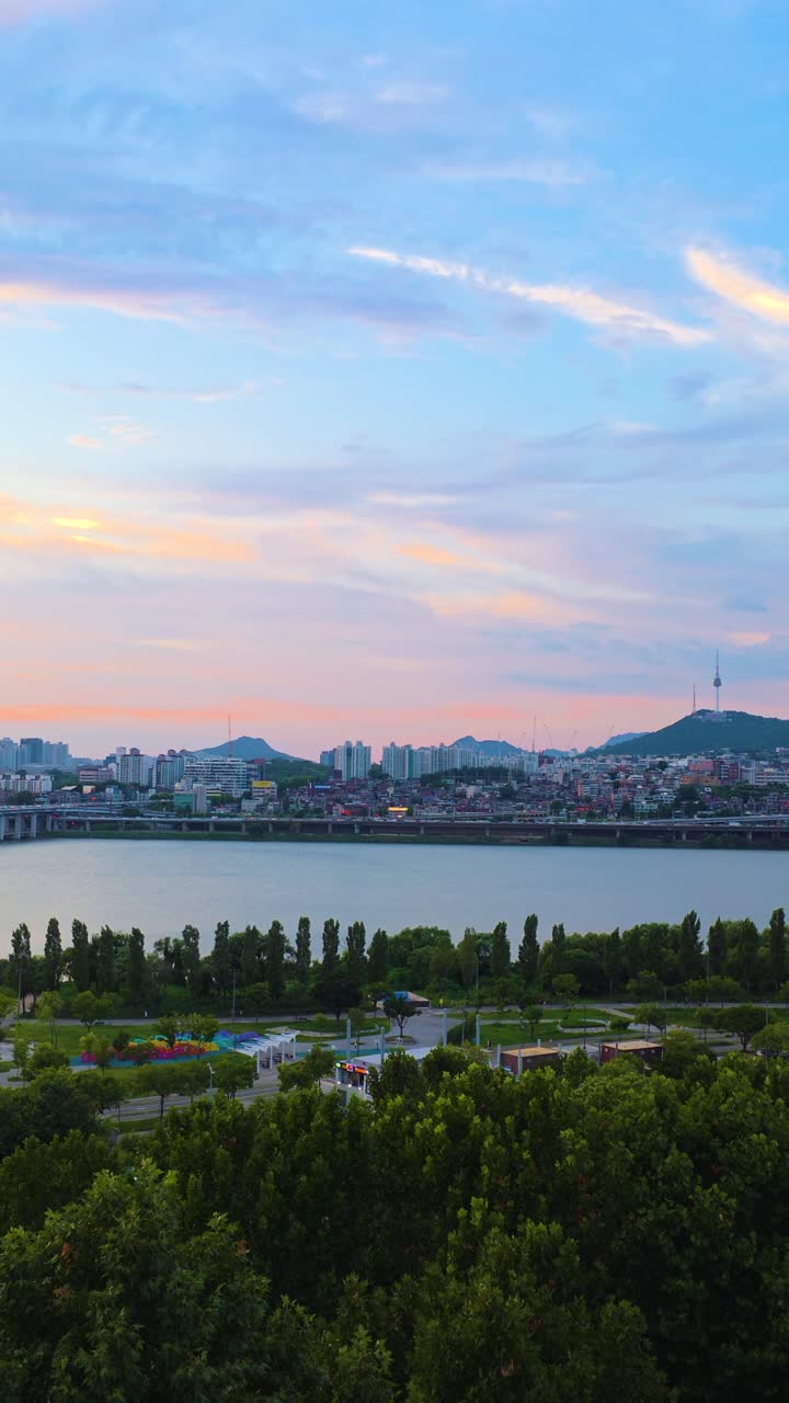 Vertical aerial zoom out captures the beautiful Han River, Namsan Tower, and Seoul's city skyline under a mesmerizing colorful sunset sky