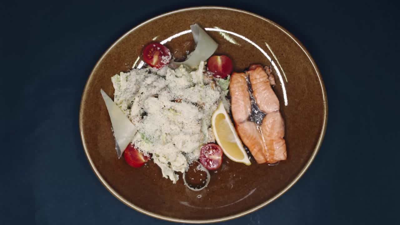 pescado rojo frito y lechuga salpicada de parmesán con una rebanada de limón en un plato sobre un fondo negro en resolución 4k