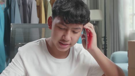 close up of asian man online seller talk on mobile phone and take note while using computer for selling clothes at home