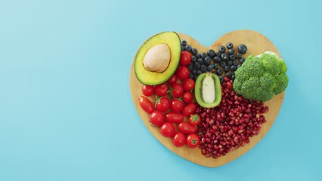 video of fresh fruit and vegetables with copy space on heart shaped wooden board on blue background