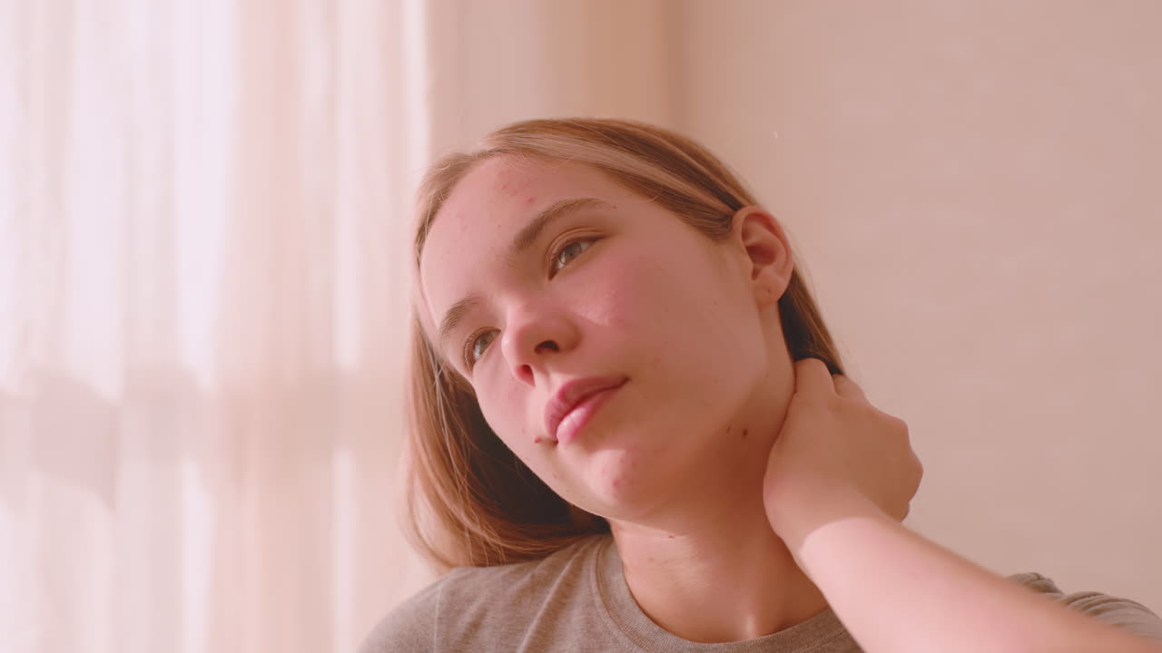 Young athlete closes eyes while gently holding neck with both hands in quiet indoor space lit by natural sunlight, expressing fatigue or relaxation through mindful self care body stretch