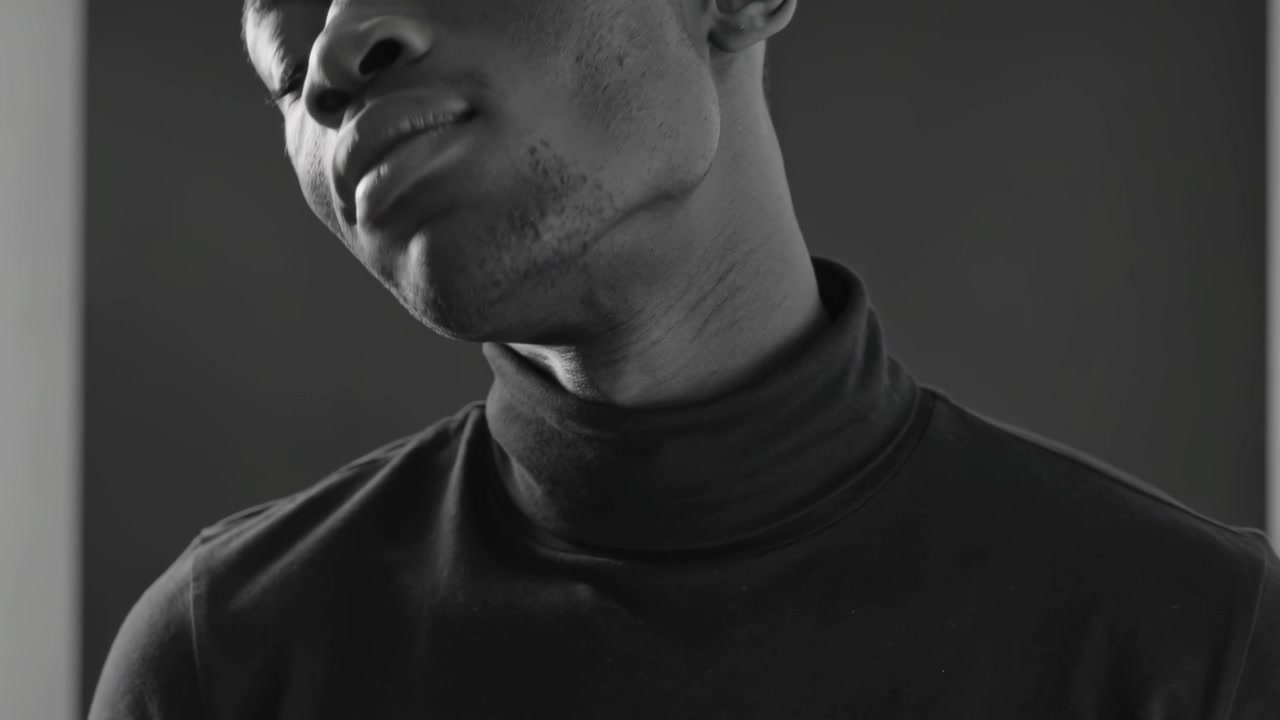 Facing camera, rotating man tilting chin showing neck in studio in dark turtleneck with light sides
