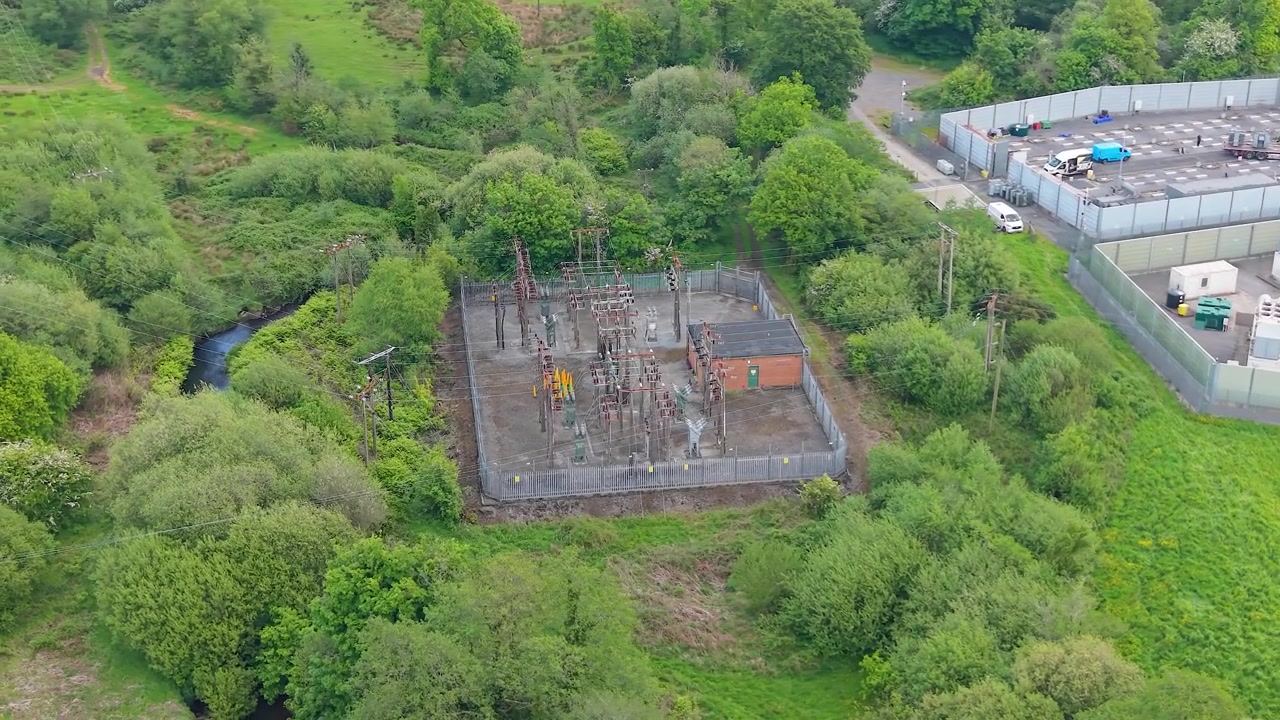 Vue aérienne large d'une sous-station électrique haute tension avec la construction d'un système de stockage d'énergie par batterie (BESS) à proximité. Infrastructure critique d'un réseau électrique moderne, distribution d'énergie, ingénierie industrielle. 4K
