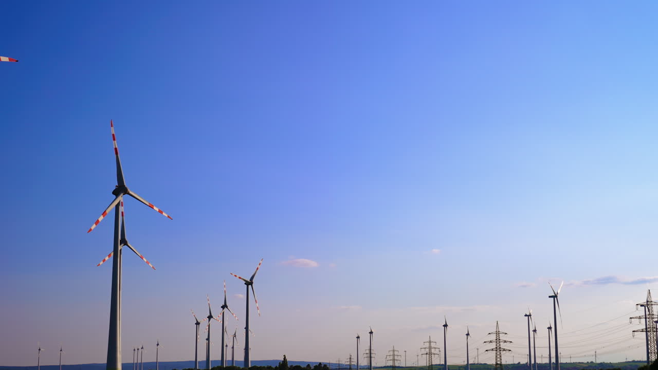 Numerous windmills rotate in the wind. Low angle view at the wind turbines at the backdrop of clear blue sky.