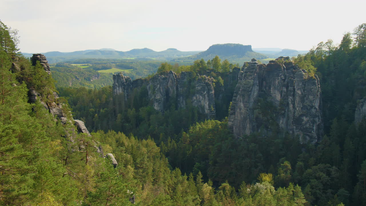Sandstone formations Elbsandsteingebirge Sachsen Elbe rising above dense green forests Mountains, under a blue sky with scattered clouds, showcasing the region’s natural beauty and rugged Terrain
