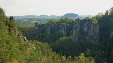 sandstone formations elbsandsteingebirge sachsen elbe rising above dense green forests mountains, under a blue sky with scattered clouds, showcasing the region’s natural beauty and rugged terrain
