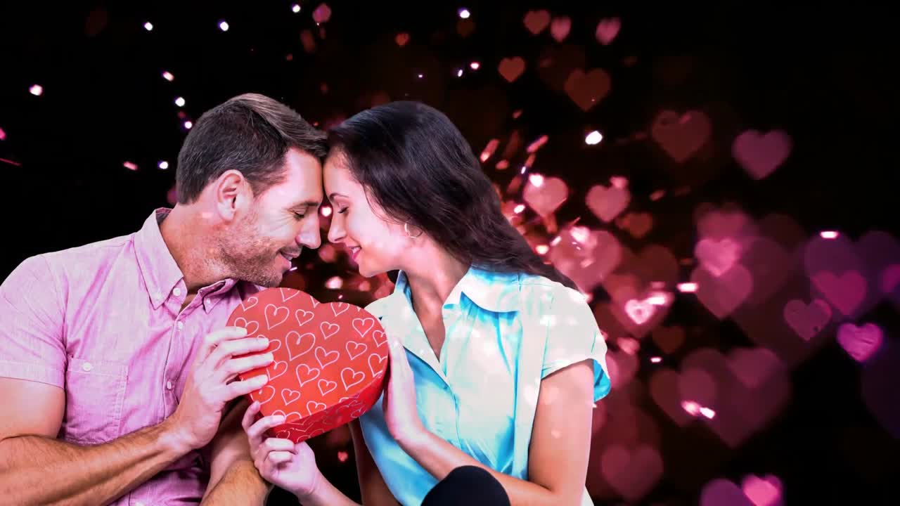 pareja enamorada tocando las frentes y sosteniendo una caja de chocolates