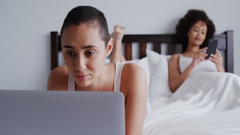 lesbian couple using laptop and mobile phone in bedroom