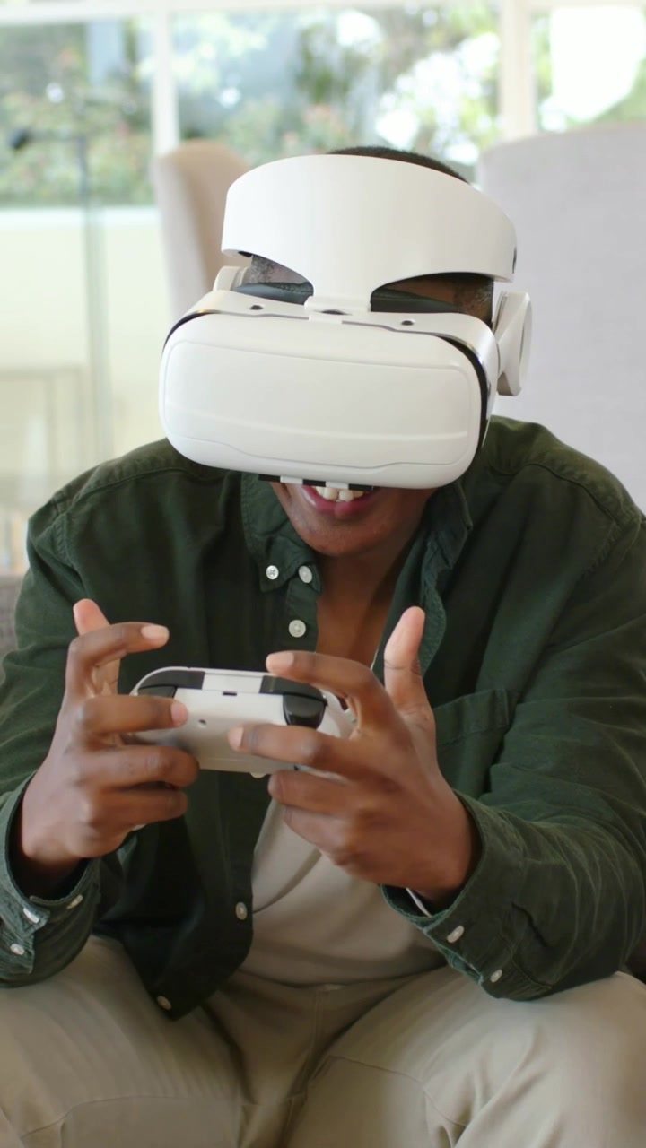 Video verticale: Uomo con maglietta verde e visore VR bianco che gioca premendo un controller per divertimento.
