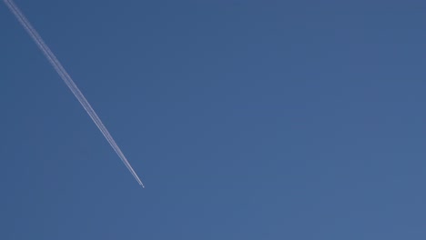 airplane flying at high altitude with contrails against clear blue sky