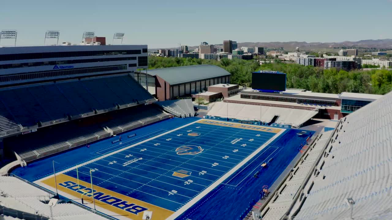 Drone shot approaching and flying into the Boise State Broncos stadium on a sunny day.