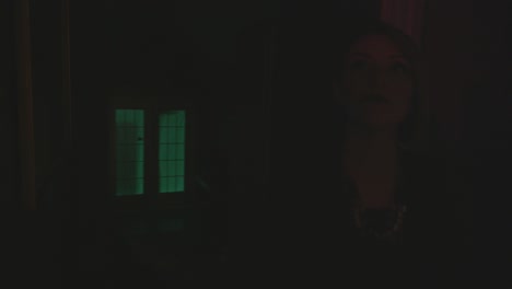 a nervous woman is walking through a house turning off lights and walking down the hallway. she seems scared while holding a book and cup in her hand