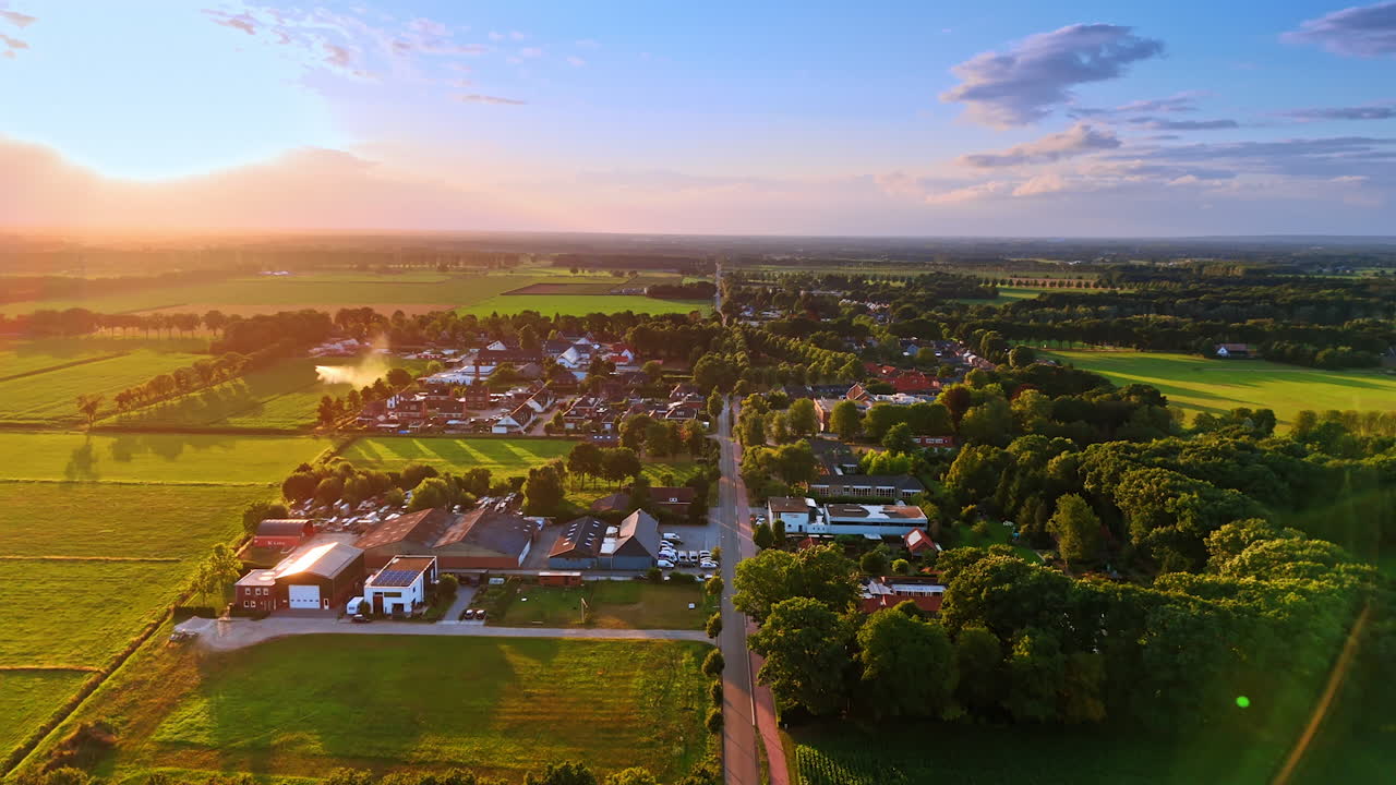 Zonsondergang boven een rustig dorp. Gouden zonlicht baadt een vredig dorp omringd door weelderige velden en bomen in de schemering, wat een serene sfeer creëert.