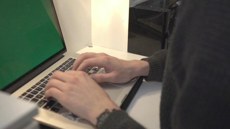Primo piano di un uomo che lavora e digita al laptop con un maglione nero.