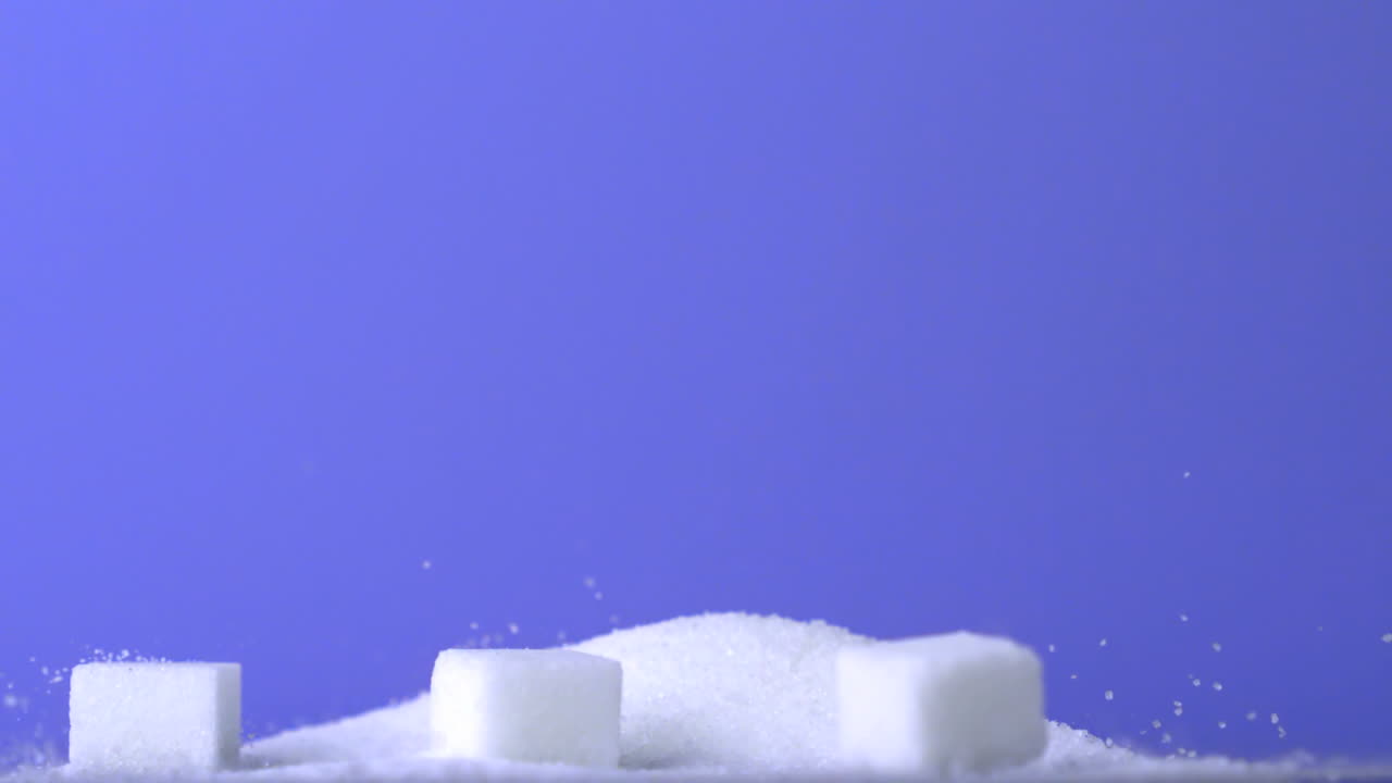 cubos de azúcar cayendo en una pila de azúcar sobre un fondo púrpura