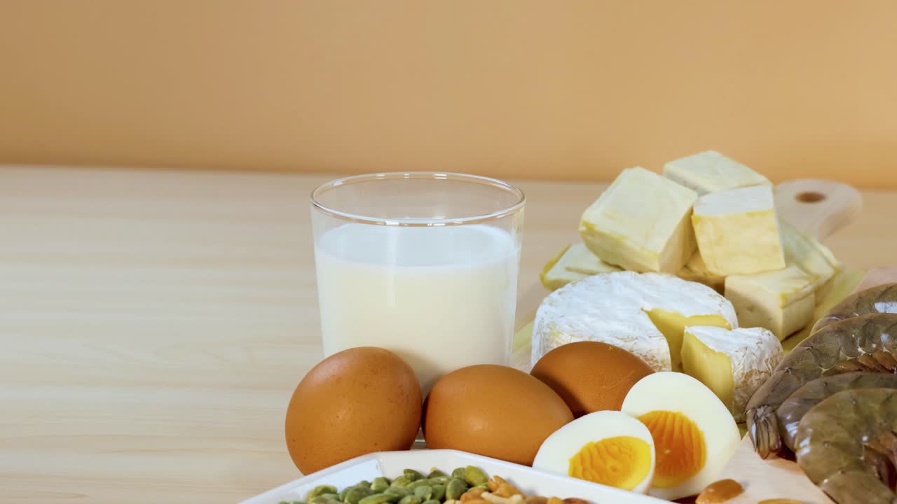 una variedad de alimentos ricos en proteínas, incluidos nueces, huevos y productos lácteos, están artísticamente dispuestos en una mesa de madera