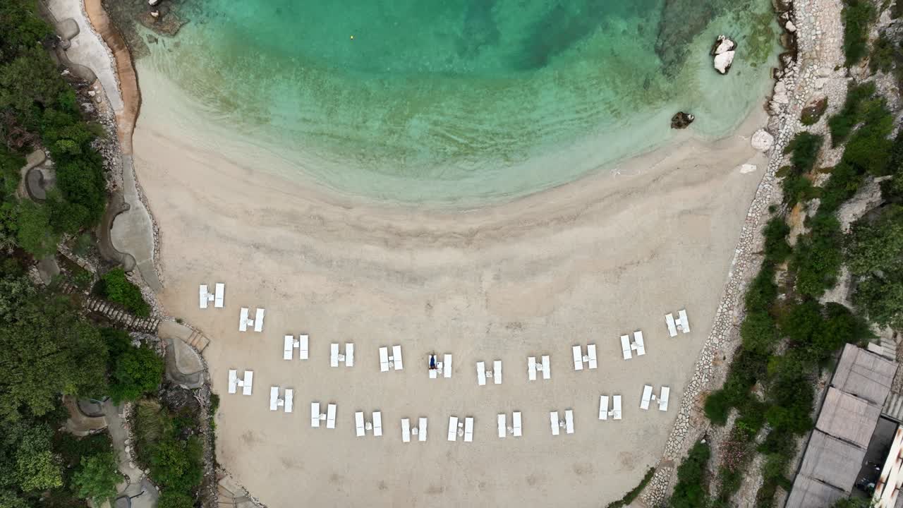 Aerial: sand beach with sunbed and turquoise water during the day in Sarande, Albania, top down drone shot