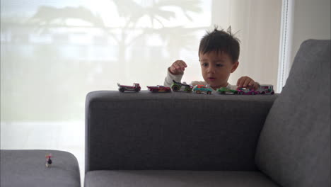 Little-hispanic-toddler-playing-with-his-car-toys-on-the-couch-on-a-cozy-morning