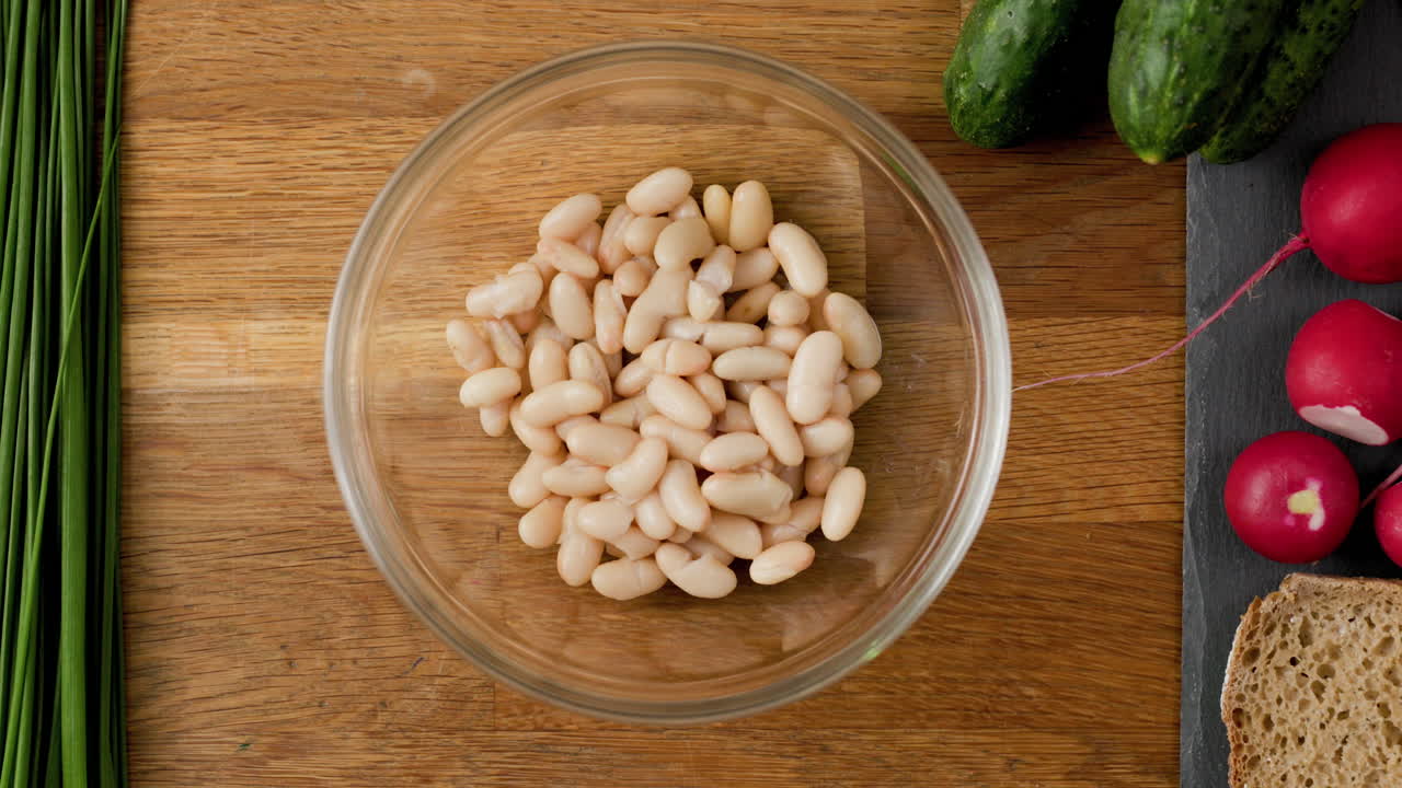 식물성 단백질로 가득 찬 채식 요리법을 준비하기 위해 테이블 위에 흰 콩이 든 유리 그릇을 밀어 넣습니다.