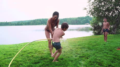 mom dad and two sons in the summer on the grass poured water from a hose for the lawn. area country house near a lake at sunset