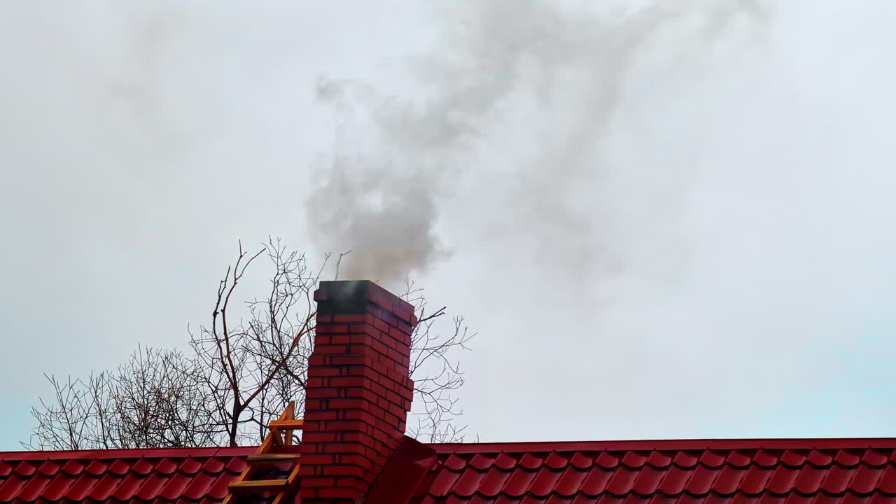 Thick smoke spew through house chimney, cherry red roof contrasting with grey gloomy sky