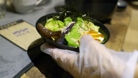 bowl full of nutritious asian vegetable and egg moved by hand on kitchen table, filmed as closeup slow motion style shot