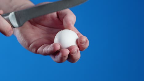 las manos de los hombres rompen un huevo crudo con un cuchillo.