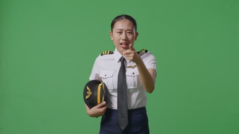 아시아 여성 조종사가 녹색 스크린 배경 스튜디오에 서서 카메라에 소리치고 있습니다.