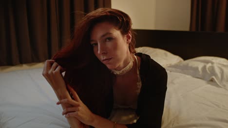 A-stunning-red-haired-woman-lies-in-bed-and-plays-with-her-hair-while-looking-up-to-the-camera