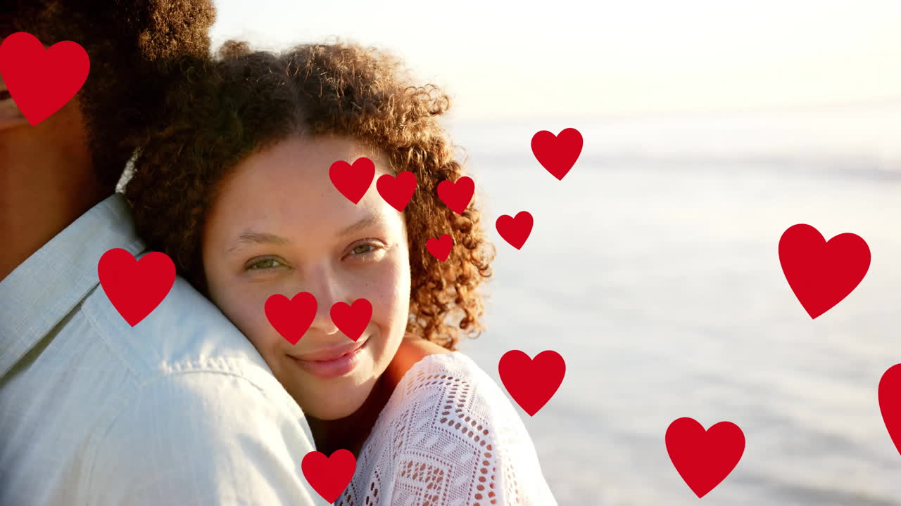 Animation of hearts moving over diverse couple in love embracing on beach in summer