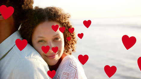 animation of hearts moving over diverse couple in love embracing on beach in summer