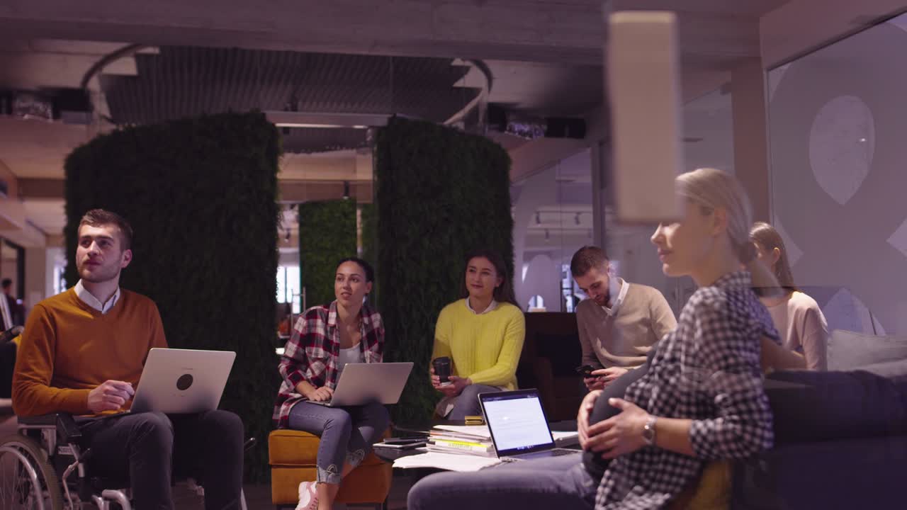 mujer musulmana en una moderna oficina de coworking de espacio abierto dando una presentación al equipo. mujer de negocios árabe de oriente medio en una oficina de startup creativa. empresario discapacitado en silla de ruedas en una reunión de equipo