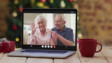 Caucasian-senior-couple-waving-on-video-call-on-laptop,-with-christmas-tree