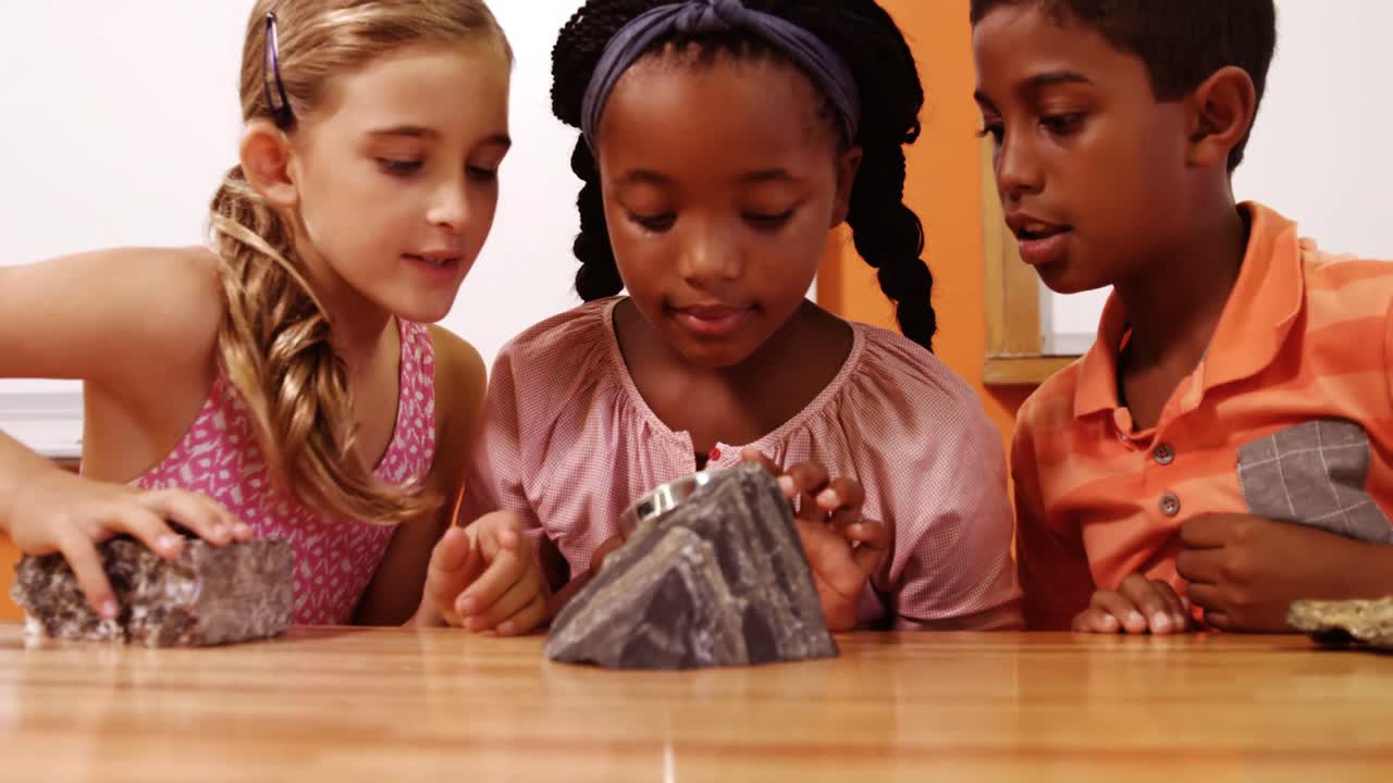 School kids using magnifying glass over rock