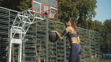 rückansicht einer sportlichen frau mit airpods, die an einem sonnigen tag auf dem basketballplatz mit ball spielt