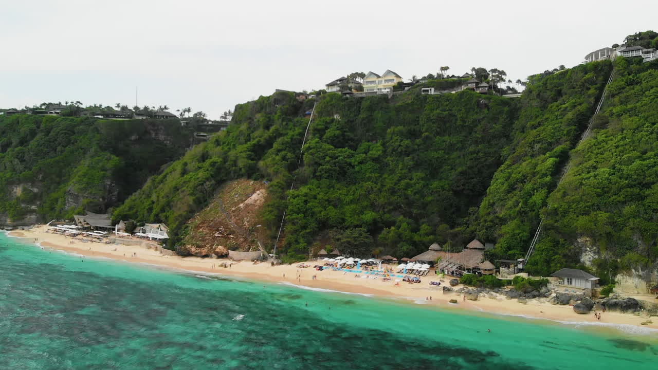 발리의 멜라스티 해변에서 숲이 우거진 절벽을 포착하는 드론 상승