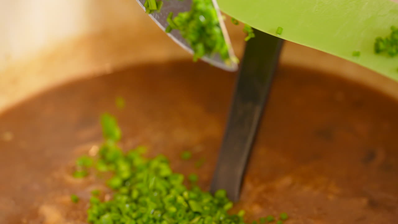 el chef arroja cebollino picado y cáscaras de lima en la sopa salada que hierve a fuego lento - cámara lenta aislada