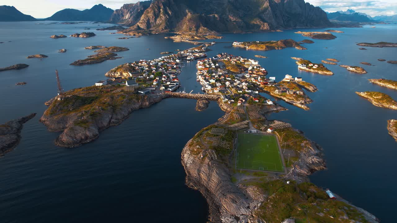 Mountain-framed fishing town of Henningsvær, Lofoten, Norway. Scenic aerial drone footage. Blue sky.