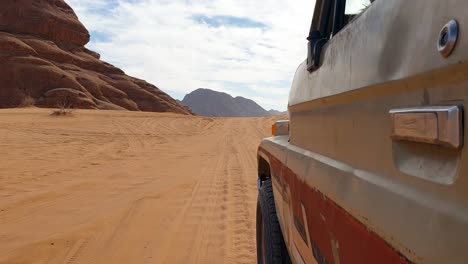 side of old 4wd truck driving through arabian wadi rum desert with red sandy, rugged mountainous landscape in jordan