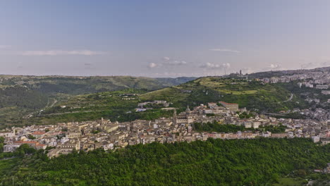 Drone-Cinematográfico-Aéreo-V2-De-Ragusa-Italia-Sobrevuela-El-Valle,-Capturando-Un-Amplio-Paisaje-De-Terreno-Montañoso-Y-El-Encantador-Paisaje-Urbano-De-La-Ciudad-De-Ibla-En-La-Ladera-Durante-El-Día---Filmado-Con-Mavic-3-Cine---Junio-De-2023