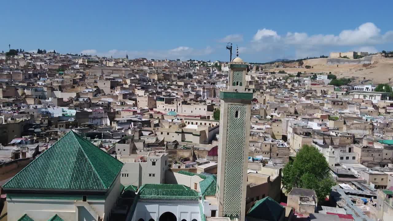 Focused drone shot of the historic Al-Qarawiyyin mosque minaret. Captures the iconic green roofs and a sweeping view of the ancient Fez medina, home to the world's oldest active university