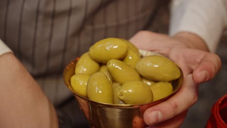 chef puts green olives into bronze metal cup with hand