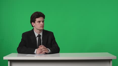 news anchor sitting at desk in front of green screen