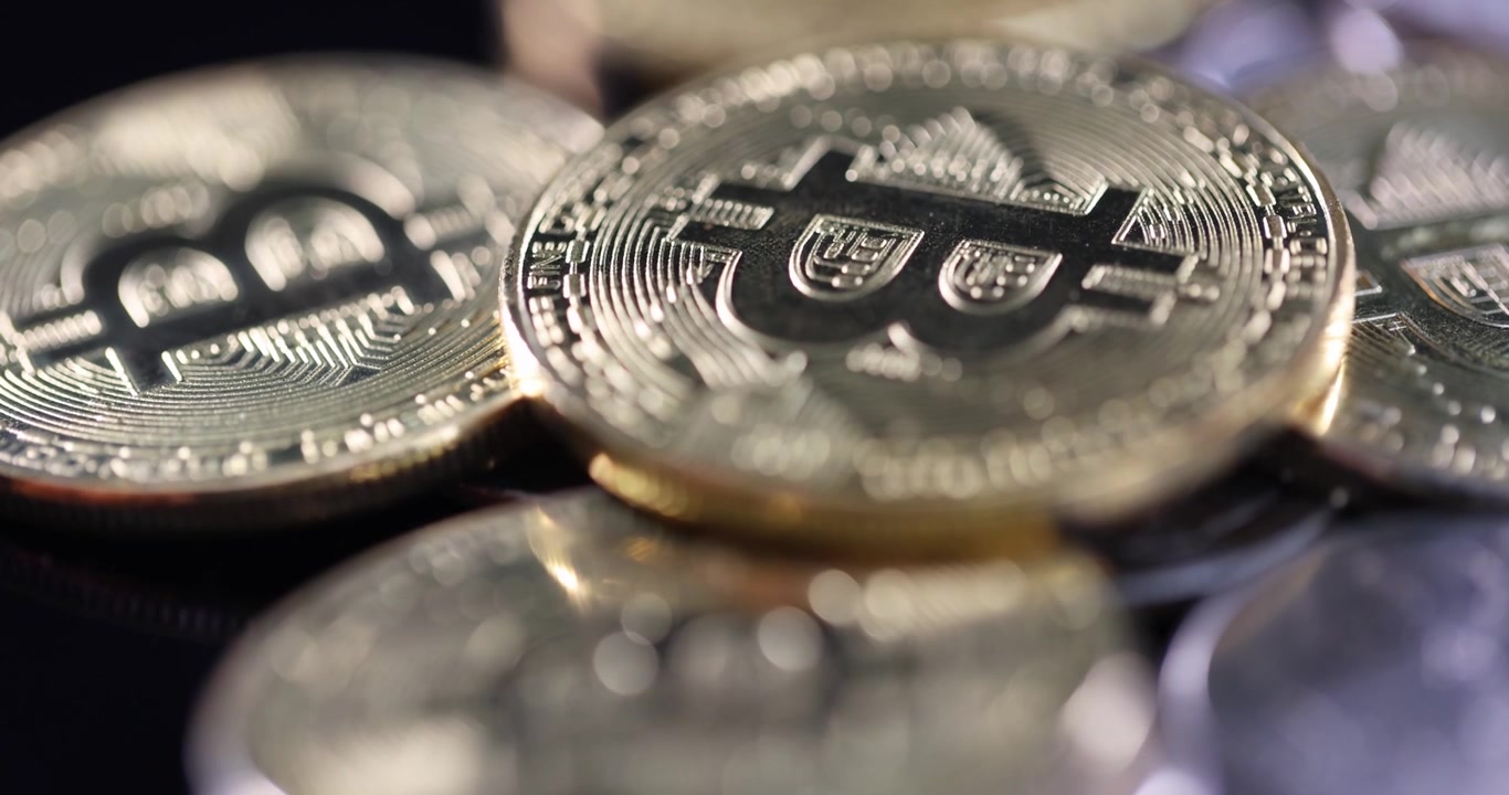 Bitcoins físicos brillantes apilados y dispersos sobre una superficie oscura.