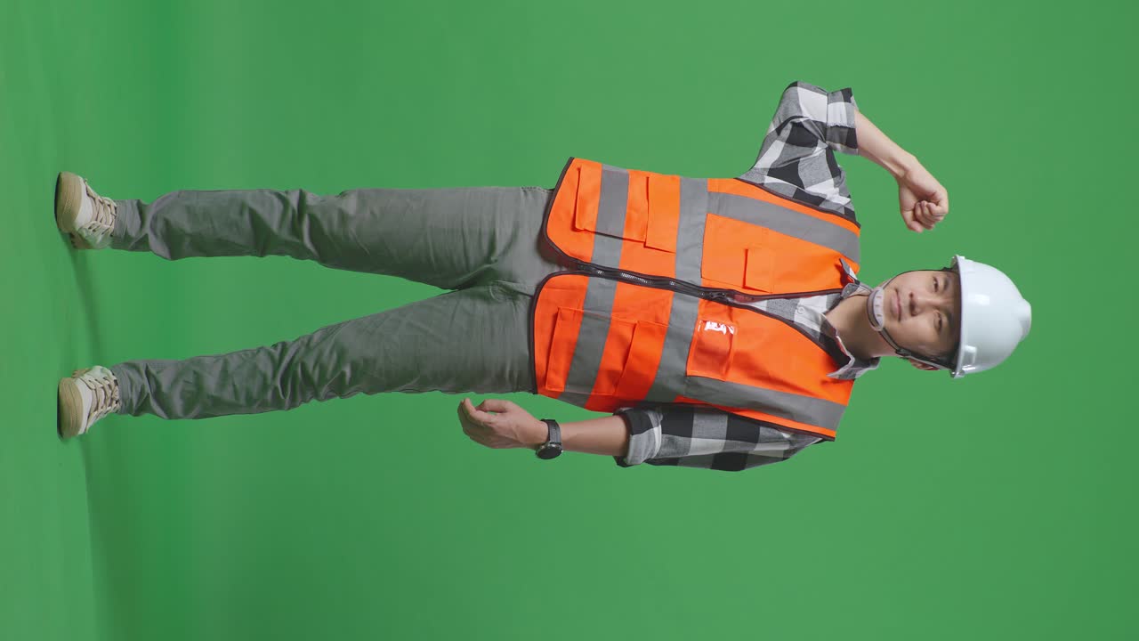 Full Body Of Asian Male Engineer With Safety Helmet Flexing His Bicep And Smiling To Camera While Standing In The Green Screen Background Studio