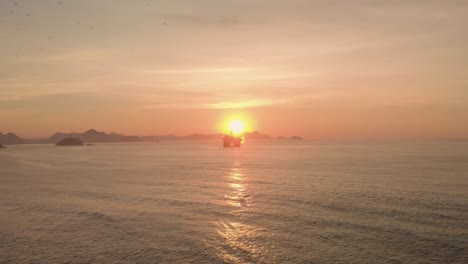 slow aerial approach of an oil platform outside of the rio de janeiro coastline in copacabana facing towards the sun