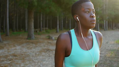 female athlete listening music while exercising in forest 4k