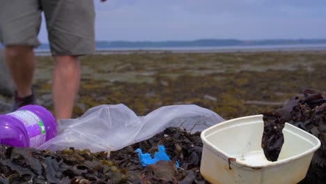 el hombre pasa junto a la basura en la playa con algas y colinas en el horizonte